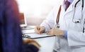 A doctor is writing a medical prescription for his patient, while sitting together at the desk in the sunny cabinet in a Royalty Free Stock Photo