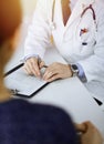 A doctor is writing a medical prescription for his patient, while sitting together at the desk in the sunny cabinet in a Royalty Free Stock Photo