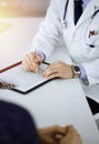 A doctor is writing a medical prescription for his patient, while sitting together at the desk in the sunny cabinet in a Royalty Free Stock Photo