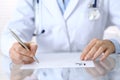 Doctor writing prescription form while sitting at glass desk in hospital, closeup view. Healthcare, insurance an