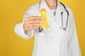 Doctor with yellow ribbon on color background. Cancer awareness concept Royalty Free Stock Photo