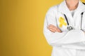 Doctor with yellow ribbon on robe against color background. Cancer awareness concept Royalty Free Stock Photo