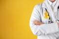 Doctor with yellow ribbon on robe against color background. Cancer awareness concept Royalty Free Stock Photo