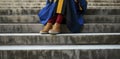 A Doctoral Graduate Clad in a Red and Blue Gown Holds a Tudor Bonnet, Casual Sneakers Completing the Look on University Steps