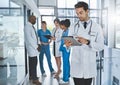 Doctoring in the digital era. a young doctor using a digital tablet in a hospital with his colleagues in the background.