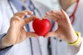 Doctors cardiologists hold red toy heart in clinic closeup