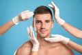 Doctors examining man`s face for cosmetic surgery on blue background