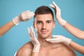 Doctors examining man`s face for cosmetic surgery on blue background