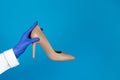 Doctors hand in a glove holds a high heels shoes on a blue background with copy space