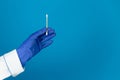 Doctors hand in a glove holds a plastic cotton swab on a blue background with copy space