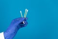 Doctors hand in a glove holds a plastic cotton swabs on a blue background with copy space