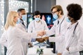 Doctors handshake in the office. Multiracial team of medical experts in protective masks, shaking hands after successful Royalty Free Stock Photo