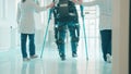 Doctors are helping a man in the exosuit to walk with crutches