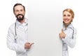 cheerful doctors holding blank banner showing thumb up and pointing with finger at copy space