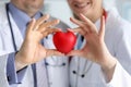 Doctors in white coats hold heart, focus on heart.