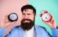 Does changing clock mess with your health. Man bearded hipster hold two different clocks. Guy unshaven puzzled face