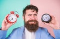 Does changing clock mess with your health. Man bearded hipster hold two different clocks. Guy unshaven puzzled face