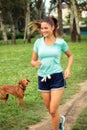 Dog following young woman while she is running in a park Royalty Free Stock Photo
