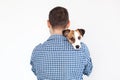 The dog lies on the shoulder of its owner. Jack Russell Terrier in his owner`s hands on white background. The concept of people an