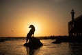 A dog silhouetted against a setting sun near a lighthouse. Royalty Free Stock Photo