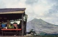 A dog sits near a make-shift hut exhibiting tropical fruit for sale set against Agung volcano of Bali. Retro 1993 film capture Royalty Free Stock Photo