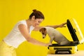 Dog is sitting in a suitcase next to a laughing woman on a yellow background. The girl is going on a trip with a pet Royalty Free Stock Photo