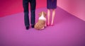 The dog is sitting between two people. Dolls from the back on a purple pink background. Text space. Human relationships, dog