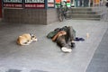 A dog sleep next to a homeless man on foot path in business area