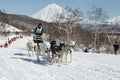 Dog team is running on snowy slopes on background of volcanoes