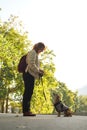 Female pet instructor in autumn clothes feeding dachshund puppy in autumn park