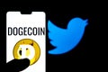 Dogecoin logo on a smartphone aganist twitter logo in the background. Dogecoin`s value has Royalty Free Stock Photo