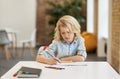 Doing assignment. Smart little school boy writing in his notebook while sitting at the desk in classroom Royalty Free Stock Photo