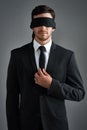 Doing business in the dark. Studio shot of a young businessman wearing a blindfold against a gray background.