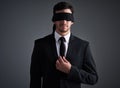 Doing business in the dark. Studio shot of a young businessman wearing a blindfold against a gray background.