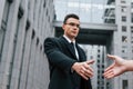 Doing handshake. Businessman in black suit and tie is outdoors in the city Royalty Free Stock Photo