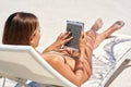 Doing a little browsing on the beach. a young woman using her tablet while relaxing at the beach.