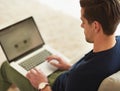 Doing a little browsing at home. High angle shot of a young man using his laptop while sitting on the sofa at home.