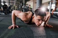 Doing push-ups. Young sportive strong man in black wear have workout day in gym Royalty Free Stock Photo