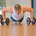 Doing some push-ups. Fit young man doing push ups in a health club using dumbbells.