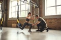 Doing squat exercise. Confident young personal trainer is showing slim athletic woman how to do squats with Trx fitness