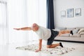 Doing yoga exercises. Funny overweight man in casual clothes is indoors at home Royalty Free Stock Photo