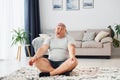 Doing yoga exercises. Funny overweight man in casual clothes is indoors at home Royalty Free Stock Photo