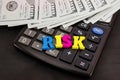 Dolars and the word `risk` from the letters lies on the calculator. Close-up. The concept of business risk, economic crisis.