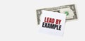 1 dollar bill and white notepad sheet on the white background. LEAD BY EXAMPLE text Royalty Free Stock Photo