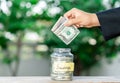 Dollar bills drop from hand in glass jar on wooden table Royalty Free Stock Photo