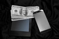 Dollar bills, an e-book and a mobile phone lie on black draped silk, modern business concept