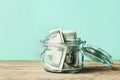 Dollar bills in glass jar on wooden table. Saving money concept.