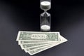 Dollar bills lie near the hourglass. Time is money. The salary. Business solutions in time. Hourglass time measurement