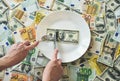 Dollar bills lie on a plate. Hand with a fork reaches for dollars