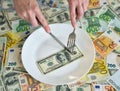 Dollar bills lie on a plate. Hand with a fork reaches for dollars